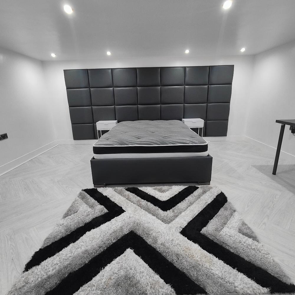 Luxurious Double Bed with Mattress and Headboard featuring a black quilted panel headboard design, paired with two white nightstands. Complete with modern recessed lighting and a striking black and white geometric rug.
