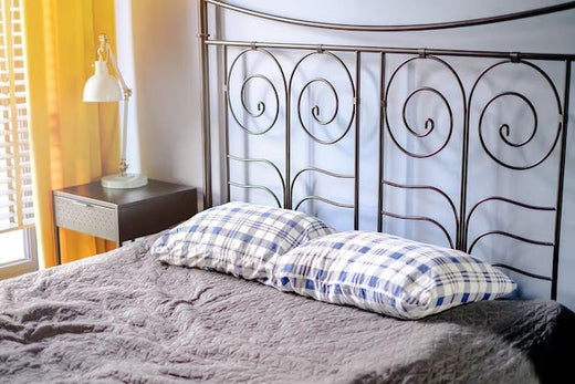 Bedroom with a metal headboard featuring swirling patterns, blue-checkered pillows, and a gray quilt.