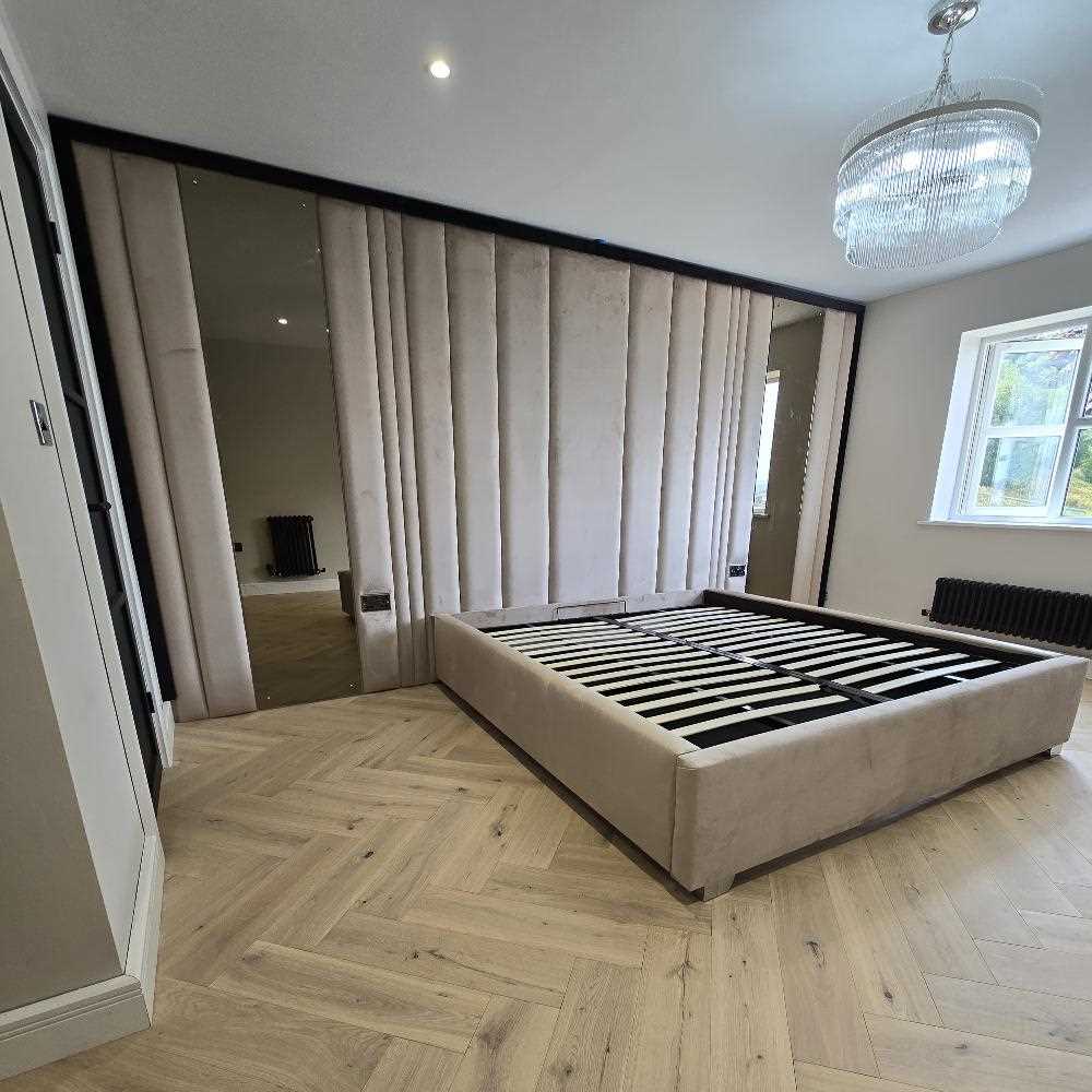 Modern bedroom with a cushioned wall bed, beige upholstery, and a chandelier.