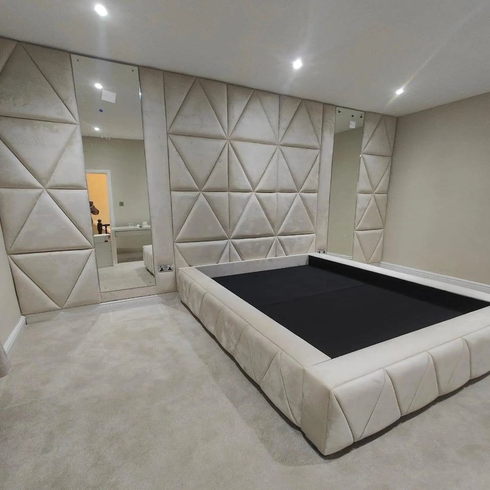 Bedroom with a beige upholstered bed frame, triangular-patterned walls, flanked by tall mirrors, and light beige carpet flooring.