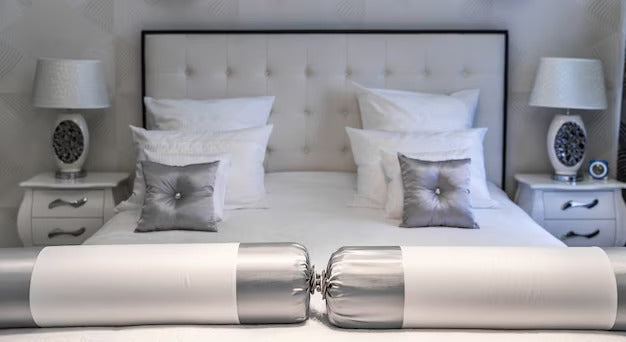 Luxurious bedroom with a super king size bed, tufted headboard, white linens, silver accent pillows, and matching nightstands with lamps.